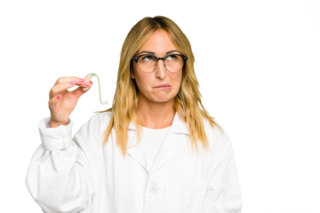 Young otorhinolaryngologist caucasian woman holding hearing aid isolated on green chroma background confused, feels doubtful and unsure.