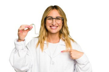 Young otorhinolaryngologist caucasian woman holding hearing aid isolated on green chroma background person pointing by hand to a shirt copy space, proud and confident