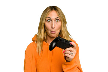 Young caucasian gamer woman holding a game controller isolated on green chroma background shrugs shoulders and open eyes confused.