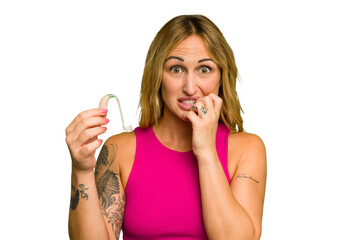 Young caucasian woman wearing hearing aid isolated on green chroma background biting fingernails,...