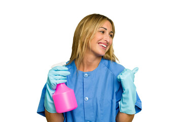 Young cleaner caucasian woman isolated green chroma background points with thumb finger away, laughing and carefree.