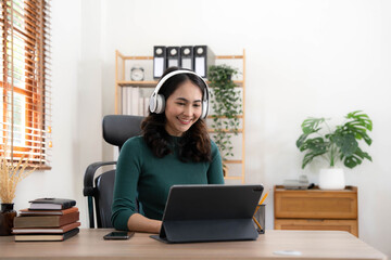 Young Asian woman wearing headphones to study online with her teacher, the girl is happy to learn.