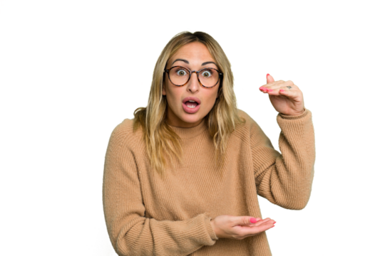 Young caucasian woman isolated on green chroma background shocked and amazed holding a copy space between hands.