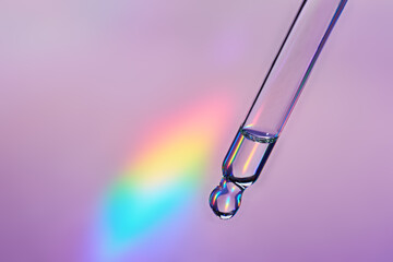 Pipette with cosmetic product on holographic background, iridescent highlights, selective focus