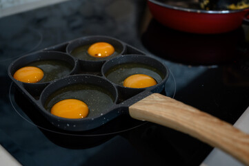 Make fried eggs on black frying pan on electric stove for breakfast.