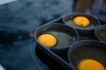 Make fried eggs on black frying pan on electric stove for breakfast.