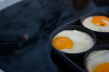 Make fried eggs on black frying pan on electric stove for breakfast.