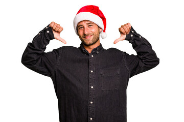 Young caucasian man celebrating Christmas wearing a santa hat isolated feels proud and self...