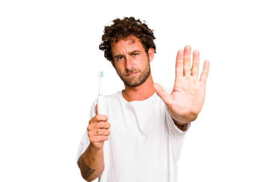 Young caucasian man holding an electric toothbrush isolated standing with outstretched hand showing stop sign, preventing you.