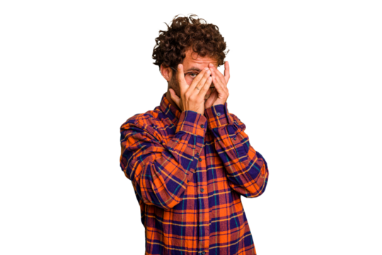 Young caucasian curly hair man isolated Young caucasian man with curly hair isolated blink at the camera through fingers, embarrassed covering face.