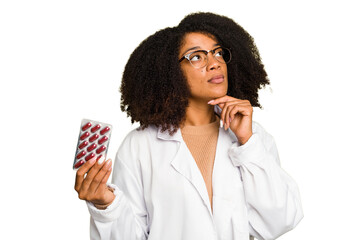 Young pharmacist African American woman holding a tablet of pills isolated looking sideways with...