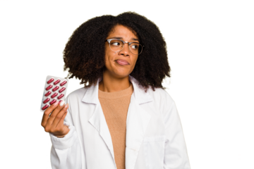 Young pharmacist African American woman holding a tablet of pills isolated confused, feels doubtful and unsure.