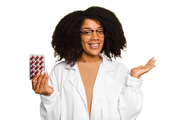Young pharmacist African American woman holding a tablet of pills isolated showing a copy space on...