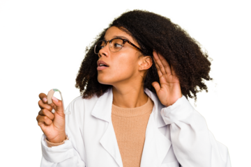 Young otorhinolaryngologist African american woman holding hearing aid isolated trying to listening a gossip.