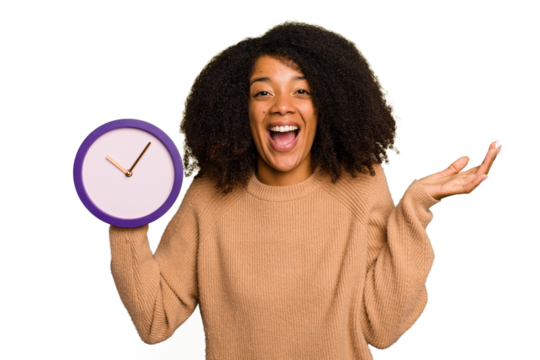 Young African American holding a clock isolated receiving a pleasant surprise, excited and raising hands.