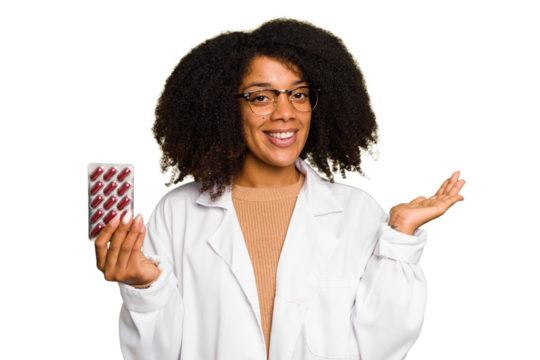Young pharmacist African American woman holding a tablet of pills isolated showing a copy space on a palm and holding another hand on waist.