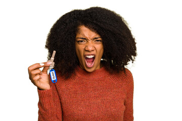 Young African american woman holding home keys isolated screaming very angry and aggressive.