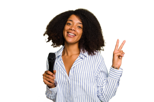 Young African American singer woman holding a microphone isolated joyful and carefree showing a peace symbol with fingers.
