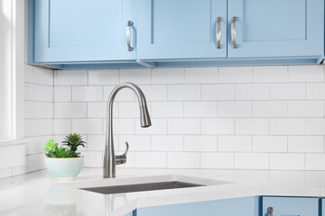 Detail of a kitchen with light blue cabinets, white granite countertop, subway tile backsplash, and...