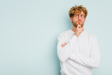 Obraz premium Young caucasian man isolated on blue background looking sideways with doubtful and skeptical expression.