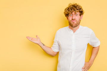 Young caucasian man isolated on yellow background showing a copy space on a palm and holding...