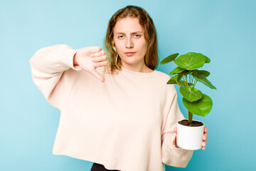 Young caucasian woman holding a plant isolated on blue background showing a dislike gesture, thumbs...