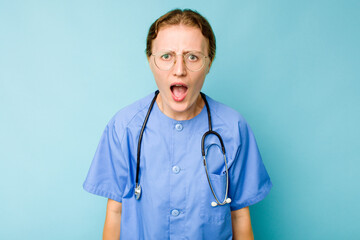 Young nurse caucasian woman isolated on blue background screaming very angry and aggressive.