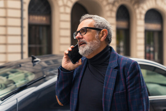 Handsome and self-confident bearded grey-haired mature businessman speaking on the phone while on his way to work. High quality photo