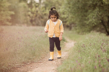 Little kid walking on a trail with a sweater and boots 