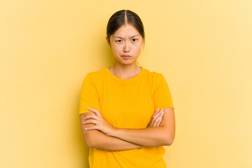 Young Asian woman isolated on yellow background frowning face in displeasure, keeps arms folded.