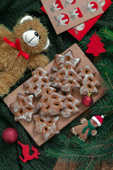 Christmas tree shaped gingerbred cookies on a wooden board on a green knitted background. Christmas composition with cookies and Christmas toys.