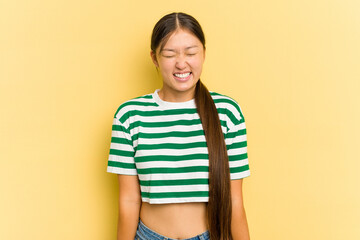 Young Asian woman isolated on yellow background laughs and closes eyes, feels relaxed and happy.