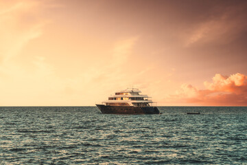Fototapeta na wymiar View of a luxury yacht floating on the waves with a stunning evening skyscape in the background; a multideck safari boat in the ocean on a sunset with a dramatic sky of a golden hour