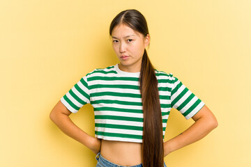 Young Asian woman isolated on yellow background frowning face in displeasure, keeps arms folded.