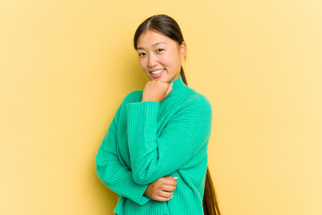 Young Asian woman isolated on yellow background smiling happy and confident, touching chin with hand.