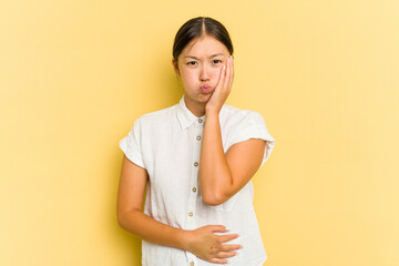 Young Asian woman isolated on yellow background blows cheeks, has tired expression. Facial expression concept.