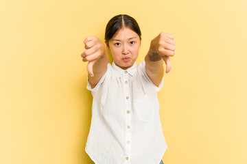 Young Asian woman isolated on yellow background showing a dislike gesture, thumbs down....