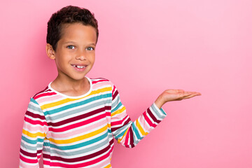 Photo of cute cheerful boy with curly hairstyle dressed striped long sleeve demonstrating empty space isolated on pink color background