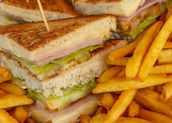 Three-tier sandwich with chicken, ham, lettuce, tomato and cheese, accompanied by French fries, also called a club sandwich