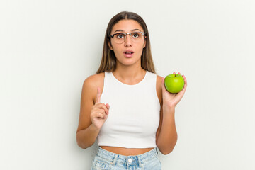 Young Indian woman holding an apple isolated on white background pointing upside with opened mouth.