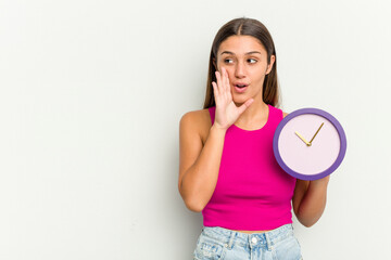 Young Indian woman holding a clock isolated on white background is saying a secret hot braking news and looking aside