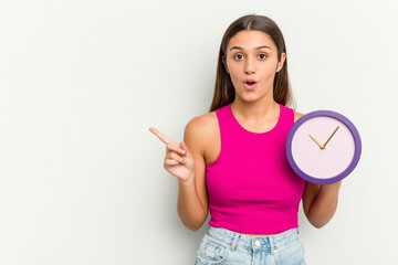 Young Indian woman holding a clock isolated on white background pointing to the side