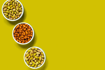 Green and yellow organic beans in three bowls on a green background. Copy space. Top view.