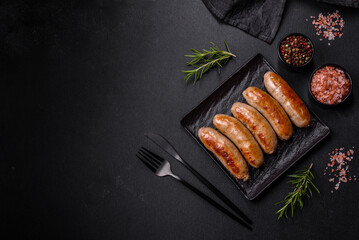 Tasty grilled sausages with spices and herbs on a black slate plate