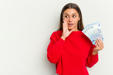 Young Indian woman holding a banknotes isolated on white background is saying a secret hot braking news and looking aside