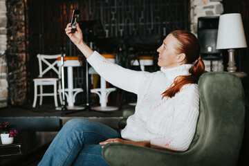 A middle-aged woman in a white sweater and blue jeans sits in a chair in the lobby of a hotel or...