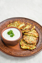 Zucchini fritters, vegetarian zucchini pancakes, served with fresh herbs and sour cream, top view. Light background.