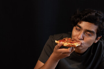 young man biting into a slice of pizza and making a face of extreme pleasure.