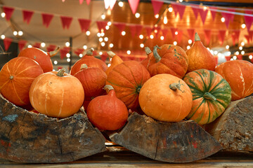 autumn harvest concept. Bunch of appetizing orange pumpkins on wood, backdrop bokeh blurred light bulbs and red flags. Festival, thanksgiving day, helloween, counter for sale, Horizontal, front view
