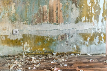 Pieces of paper wallpaper and rubbish are scattered on the floor near a wall with cracked plaster and a European socket. Template with copy space for apartment renovation
